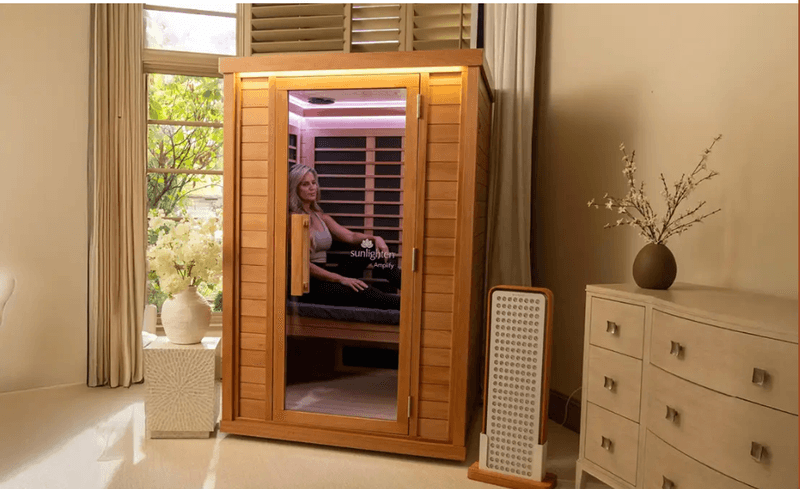 A woman resting inside a Sunlighten infrared cabin sauna in a softly lit bedroom